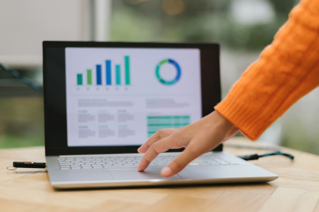 グラフや表を写したノートパソコンのマウスパッドの上に女性が手を載せている画像
